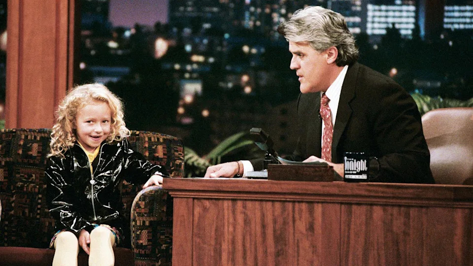 Actress Hayden Panettiere, who has curly blonde hair and wears a black shiny jacket, during an interview with host Jay Leno on October 3, 1996