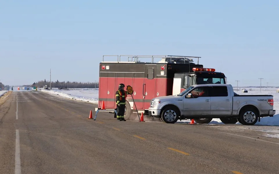 Firefighters at roadside with fire truck and pickup truck amid snowy landscape, setting safety cones on a rural highway