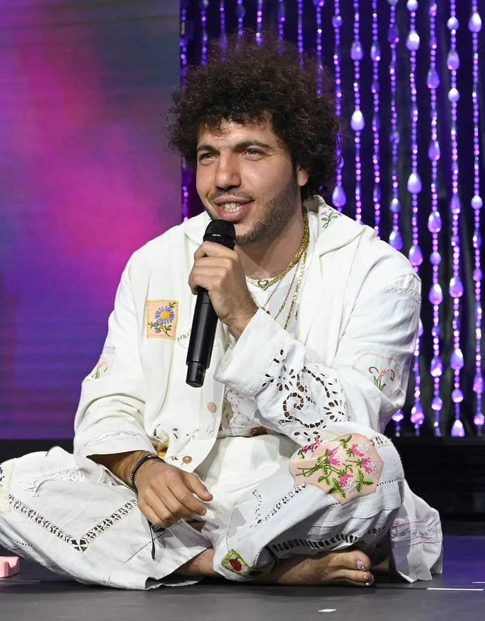 Benny seated on stage holding a microphone