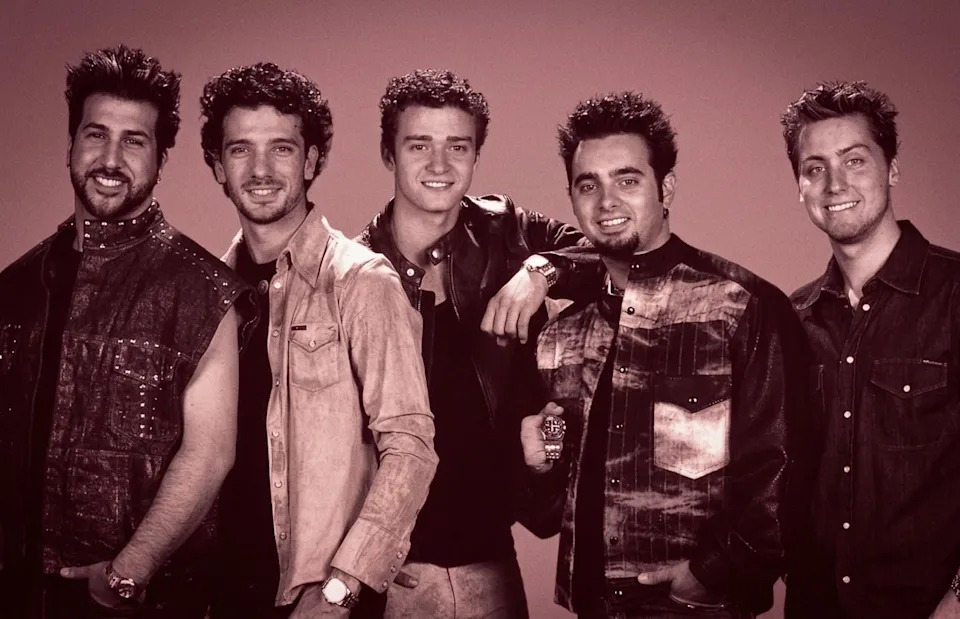 A group photo of *NSYNC members in casual outfits against a yellow background.