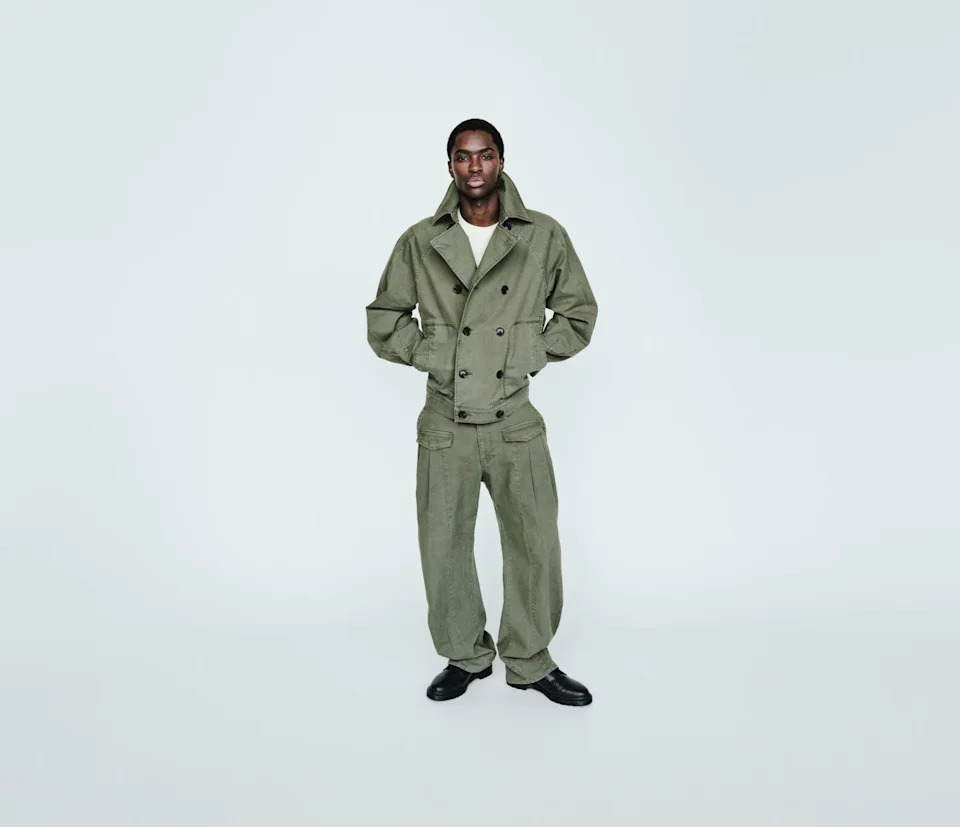 A model wearing an olive green double-breasted jacket and matching pants against a plain background.