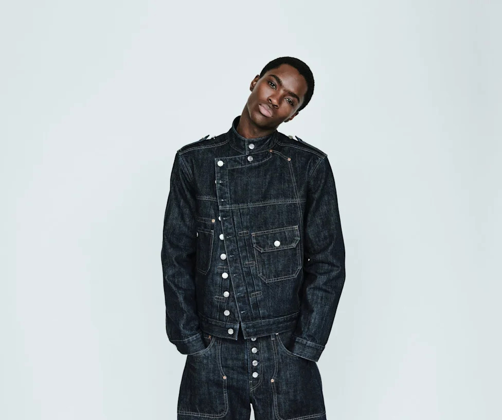 Model wearing a dark denim jacket and pants, posed against a plain background.