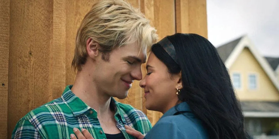 Man with blonde hair in green plaid shirt and woman with black hair in blue shirt smiling at each other.