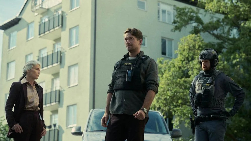 Three people stand in front of a building; Jakob Oftebro in police gear, a woman in business attire, and another officer.
