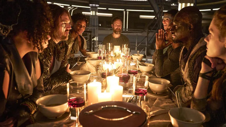 A group of space officers around a table eating heartily in Beacon 23