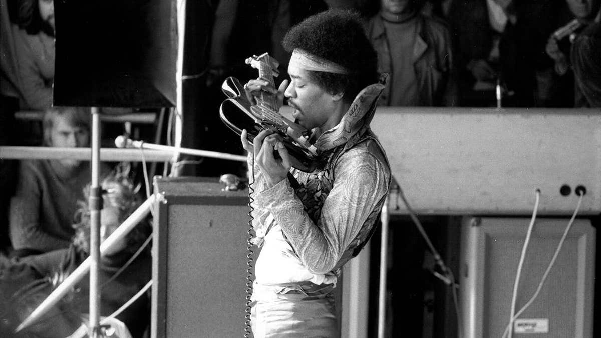 Jimi Hendrix plays electric guitar with his teeth onstage.