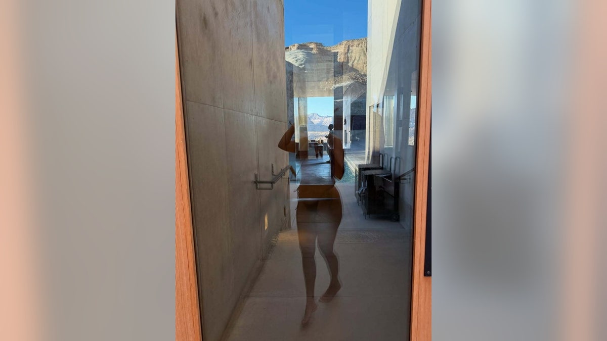 Kourtney Kardashian's silhouette appears reflected in a glass door with a desert landscape visible in the distance.