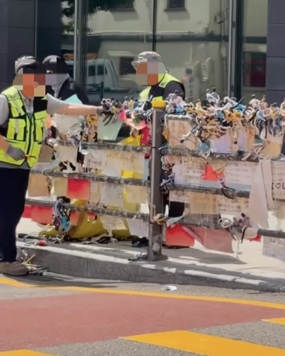 Local sanitation workers remove dolls, letters and other fan items from pedestrian railings outside HYBE’s headquarters in Yongsan-gu, Seoul. (TikTok)