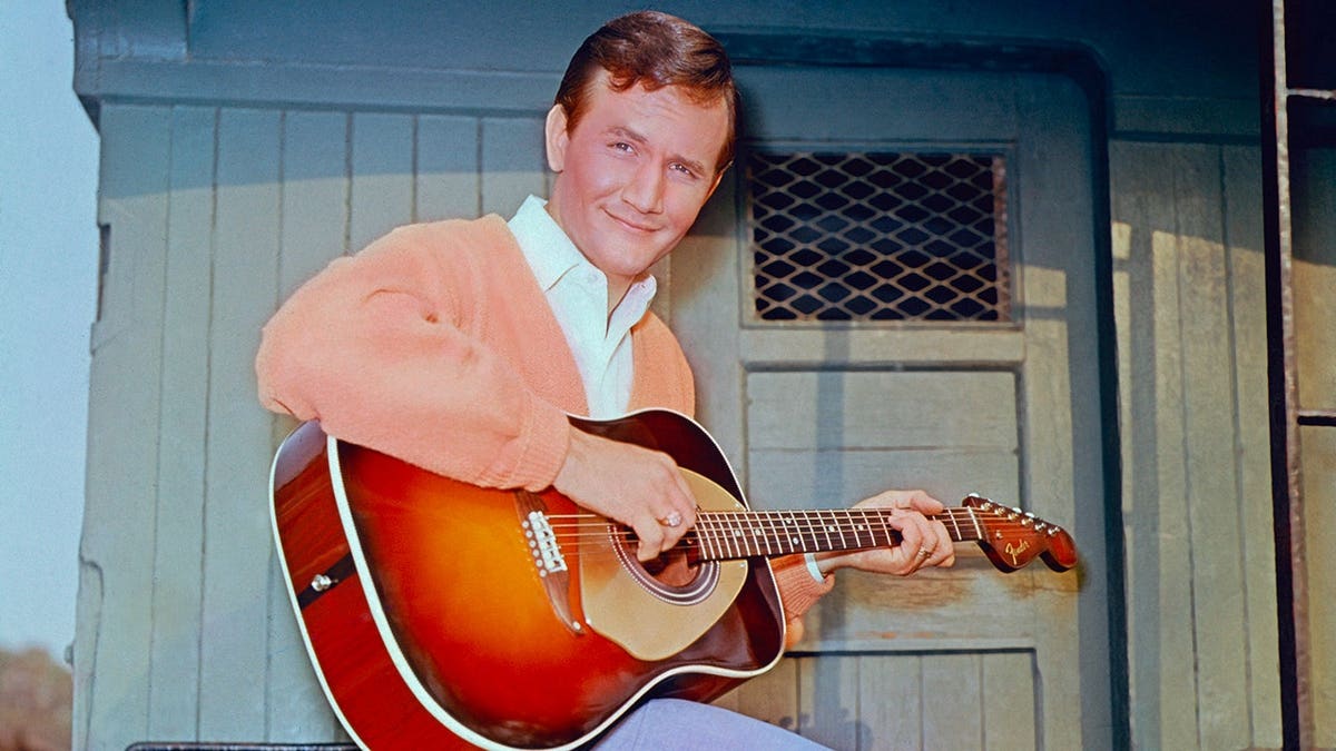 Roger Miller sitting with his guitar in 1965.