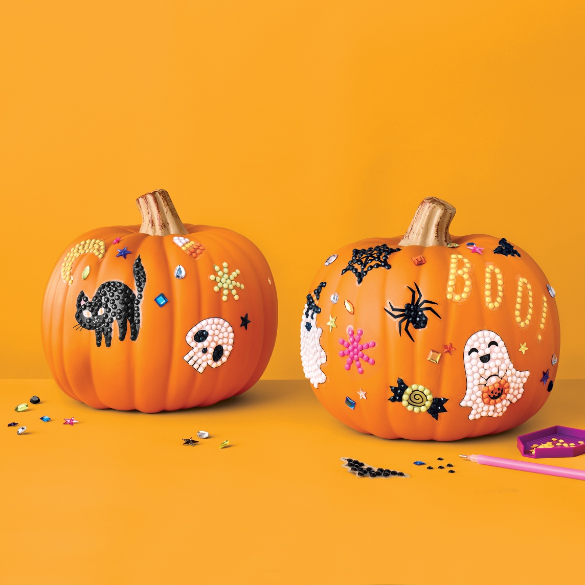 Two decorated pumpkins featuring Halloween-themed gem art designs, including ghosts, spiders, a black cat and the word "Boo."