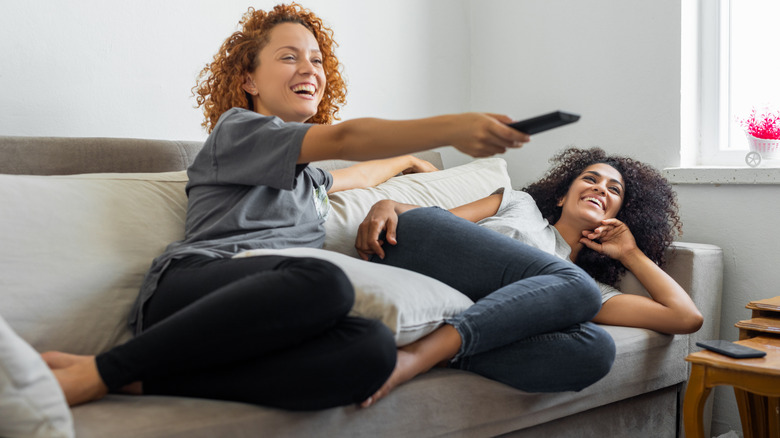 Two women lounging on a couch and watching TV
