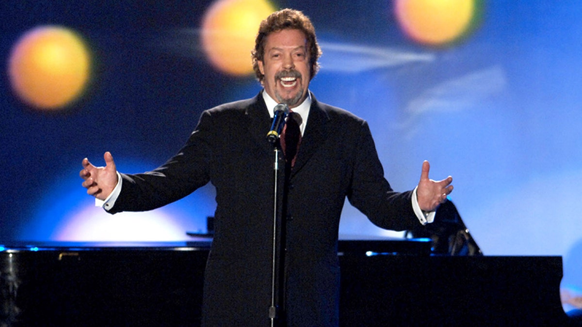 Tim Curry performs on stage with his hands out.