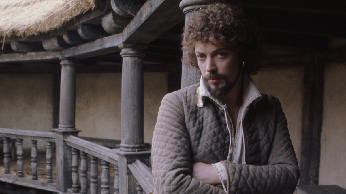 Tim Curry poses for the camera with his arms crossed on set.