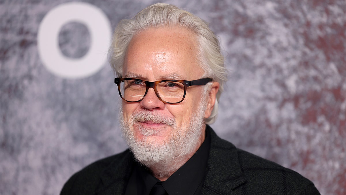 Tim Robbins poses on the red carpet at the "Silo" Season Two world premiere in front of an event backdrop.