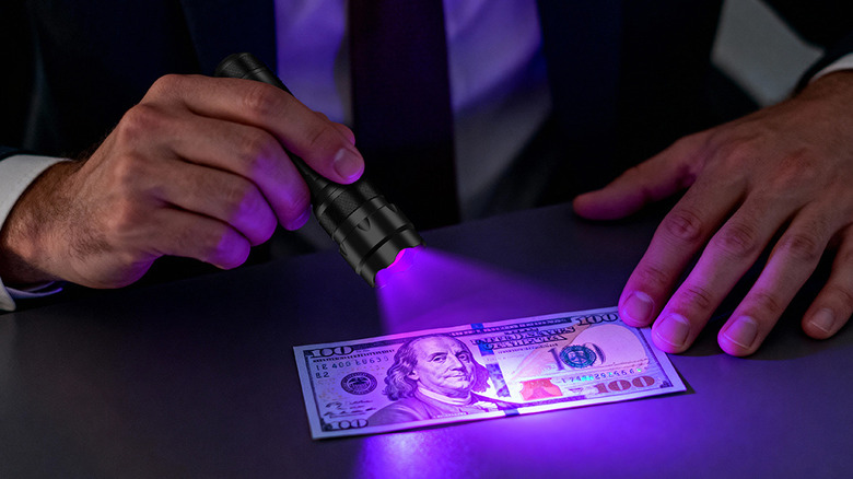 A person using the UltraFire 502UV UV flashlight on a dollar bill.