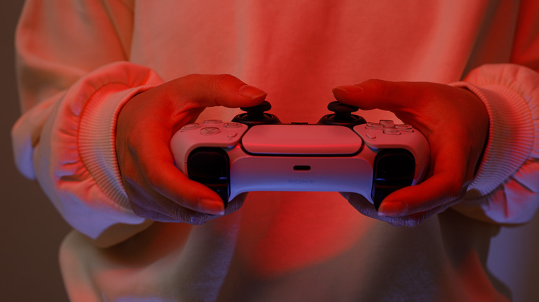 A person holding the DualSense controller, bathed in red light
