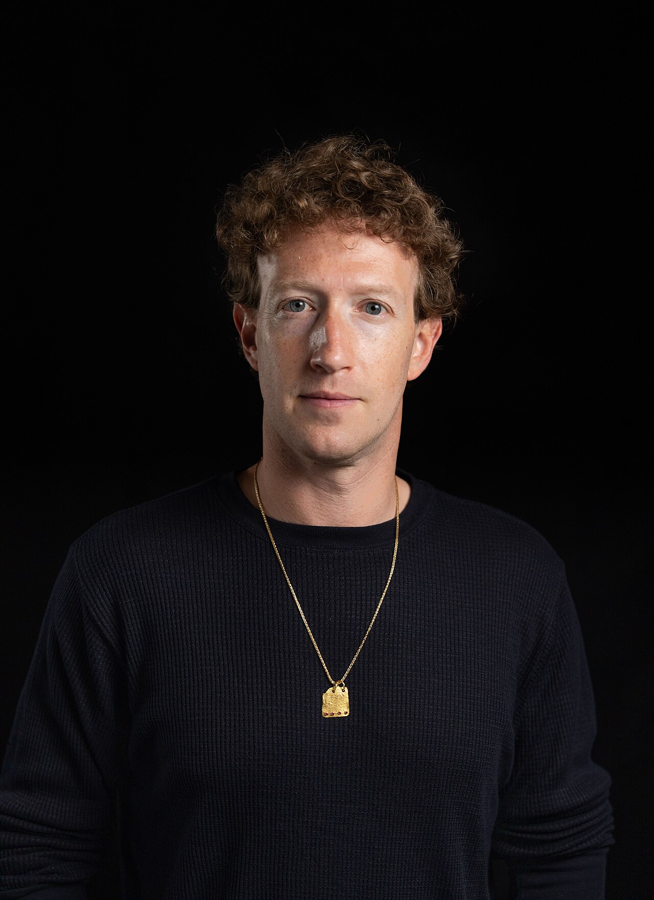Studio portrait of Meta chief executive Mark Zuckerberg against a black background, wearing a dark sweater and a gold chain