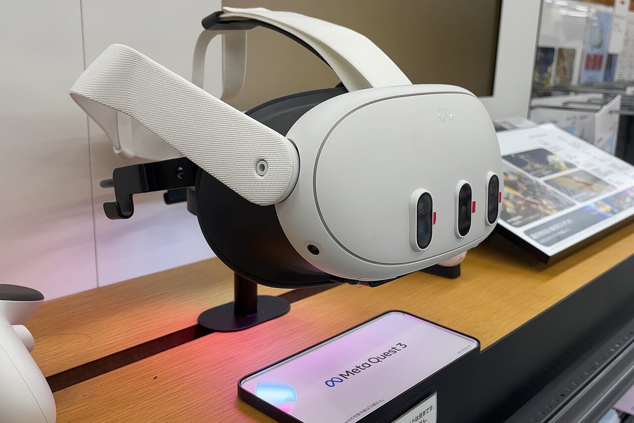 A Meta Quest 3 display unit on a retail stand, showing the three sensor housings across the front of the headset