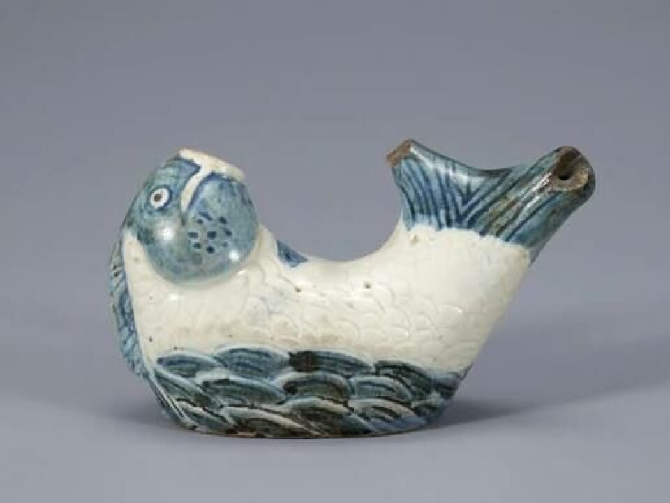 White and blue glazed ceramic fish sculpture on a gray surface.