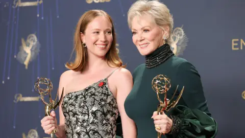 Getty Images Hannah Einbinder and Jean Smart, winners of outstanding supporting actress in a comedy Series and lead actress in a comedy series for Hacks at last year's Emmys - Einbinder is wearing an off-the-shoulder silver and black dress, while Smart is wearing a forest green high-necked dress