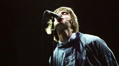 Getty Images Liam Gallagher wearing an Umbro jumper while singing into a mic during one of Oasis's famous Maine Road gigs in 1996