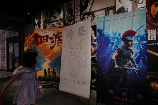 A child looks at a drawing poster promoting a Chinese animated film "Niu Lai" on display with other movie posters at a cinema in Beijing, Tuesday, Aug. 18, 2026. (AP Photo/Andy Wong)