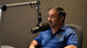 Scott Helms wearing a blue collared shirt sitting at a desk behind a microphone