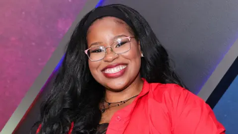 Getty Images Carla Jeffery grinning in glasses and a red blouse, posing for photos at the world premiere of Disney's Zombies 4: Dawn Of The Vampires at El Capitan Theatre on 8 July, 2025 in Los Angeles.