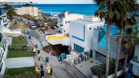 AP A large sinkhole is seen outside a mansion in Malibu, with emergency servicves attending, and palm trees and the ocean seen in the background