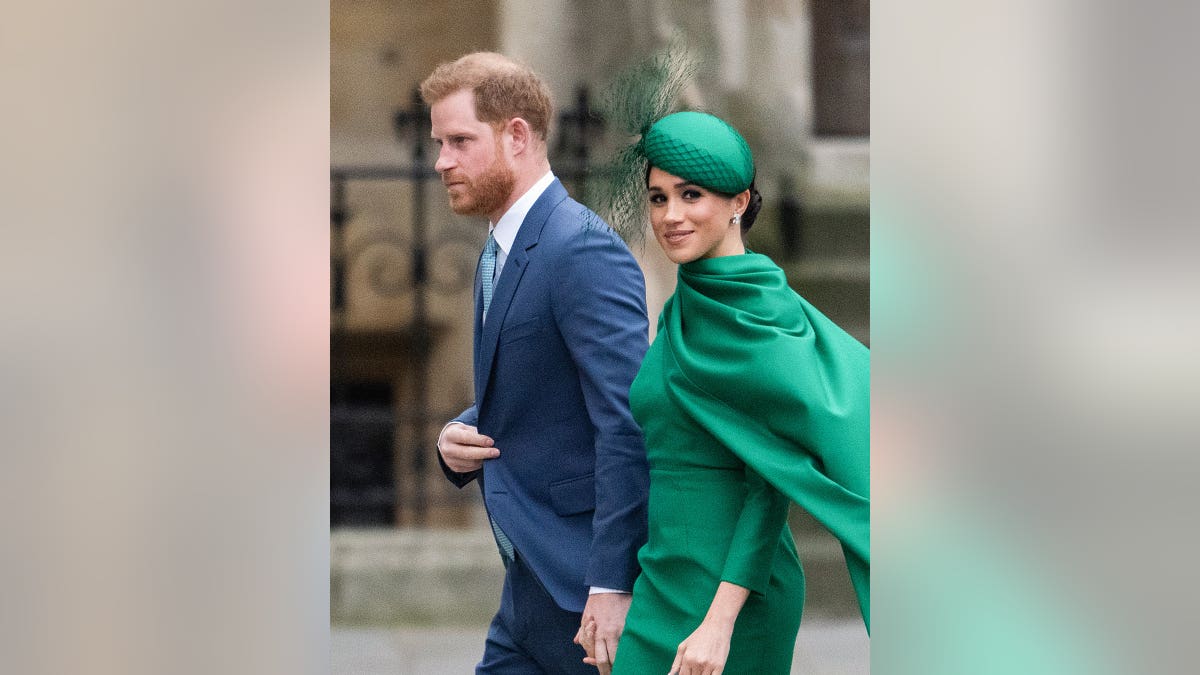 Prince Harry in a blue suit walks beside Meghan Markle in an emerald green dress and matching fascinator.