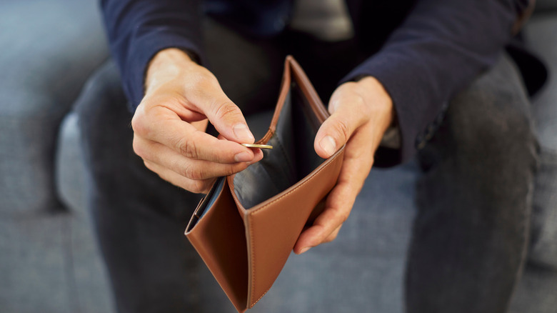 A person taking a singular coin out of an otherwise empty wallet