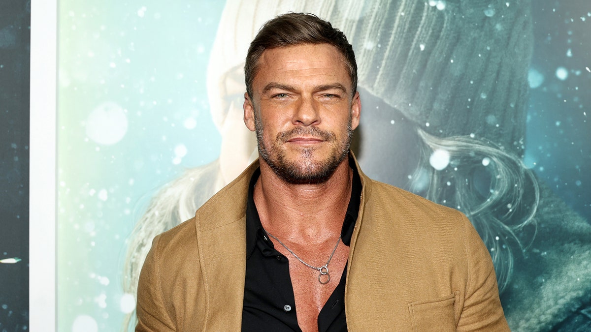 Alan Ritchson standing on a red carpet at the