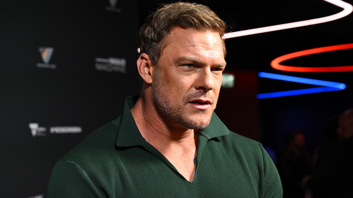 Alan Ritchson standing on a red carpet at the War Machine premiere in Melbourne.