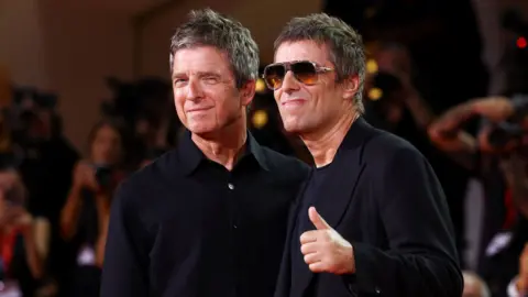 Reuters Noel and Liam smiling while on the red carpet at the Venice Film Festival ahead of the premiere of their comeback tour film, Don't Look Back in Anger. Liam is wearing shades and giving a thumbs up