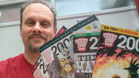 Chris Matterface A photo of a man holding different magazines up and smiling into the camera
