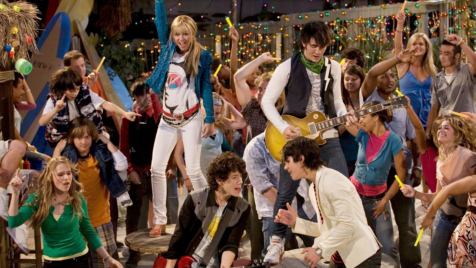 This image captures a iconic moment from the Disney Channel series Hannah Montana. Miley Cyrus (as Hannah Montana) is performing alongside the Jonas Brothers.