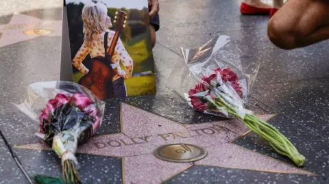 EPA A star on the pavement with Dolly Parton's name, and two bunches of red flowers and a photo laid on it