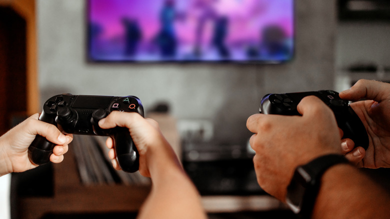 Two pairs of hands holding Xbox controllers while gaming