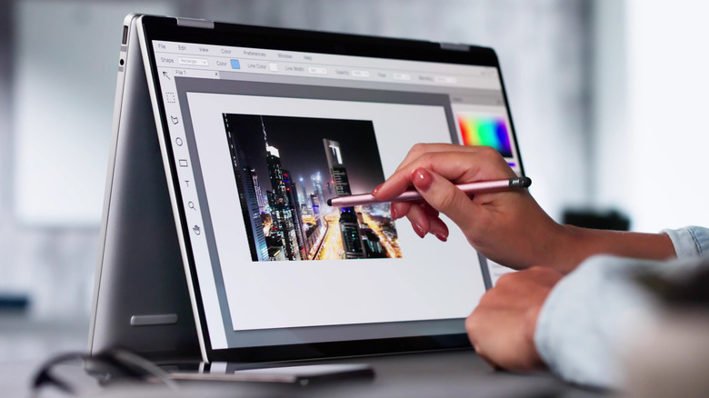 A person uses a stylus to edit photos on a convertable laptop.