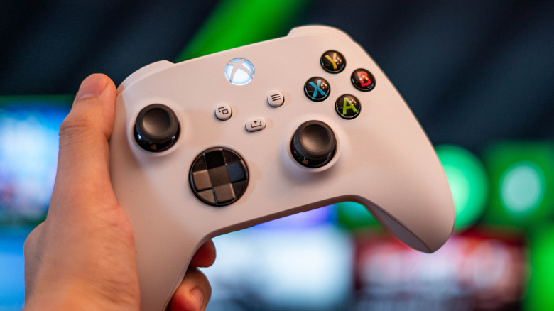 White Xbox controller held in hand with a blurred gaming background.