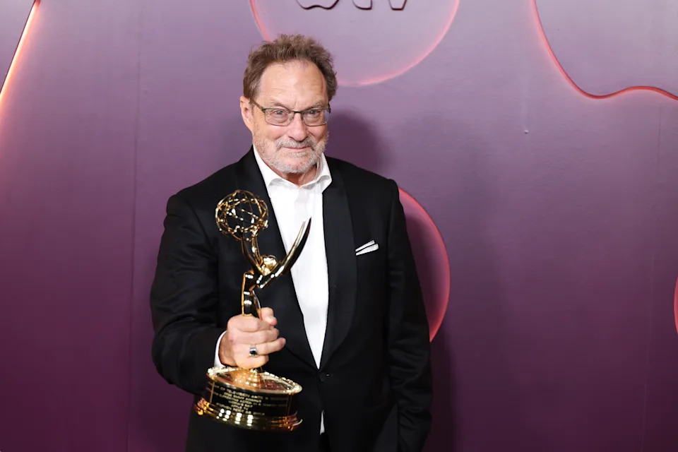 Stephen Root holding his Emmy against a purple background