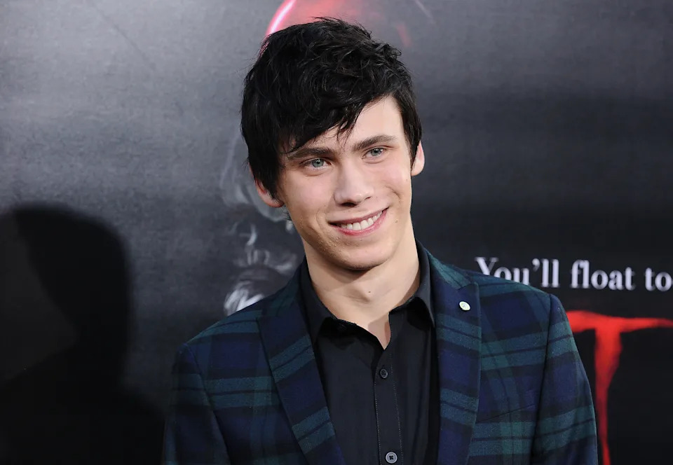 A young man in a plaid suit and dark suit smiles on the red carpet. Actor Owen Teague attends the premiere of "It."