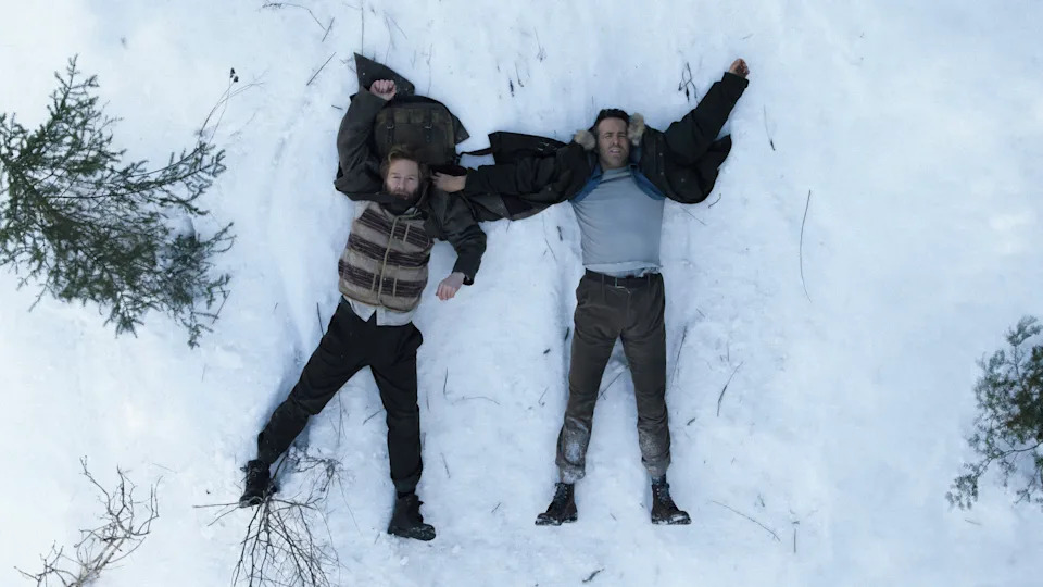 Kenneth Branagh and Ryan Reynolds in "Mayday." Two men lie flat on their backs after falling on the snow-covered ground with pained expressions on their faces.