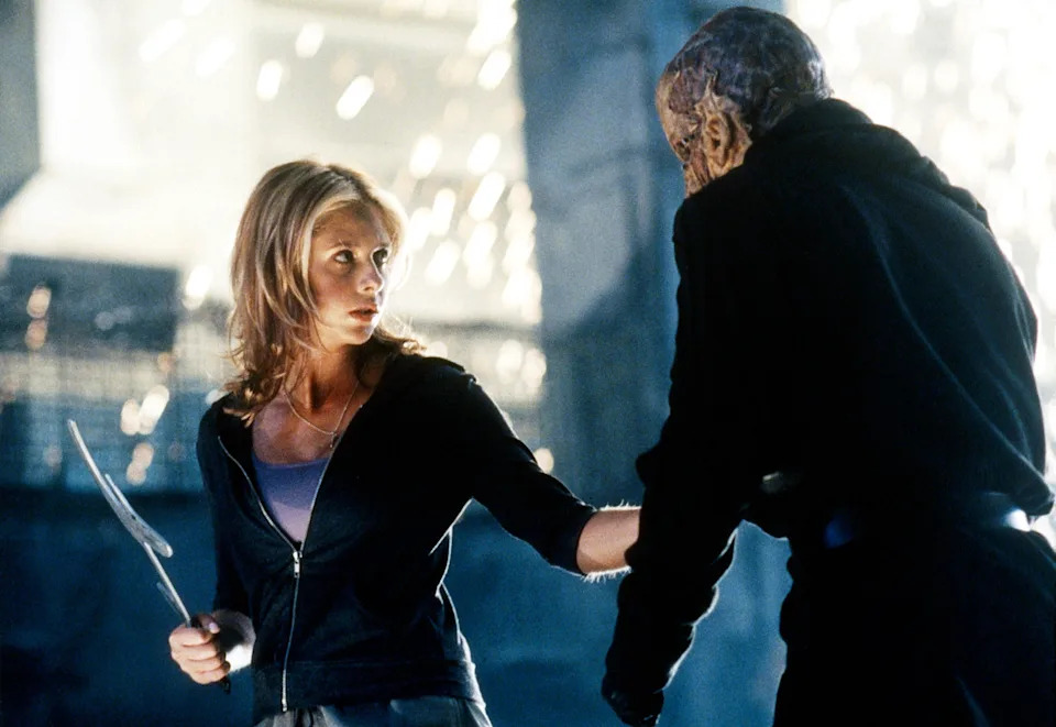 Sarah Michelle Gellar in Buffy the Vampire Slayer. A young woman holds a sword as she fights a male zombie.