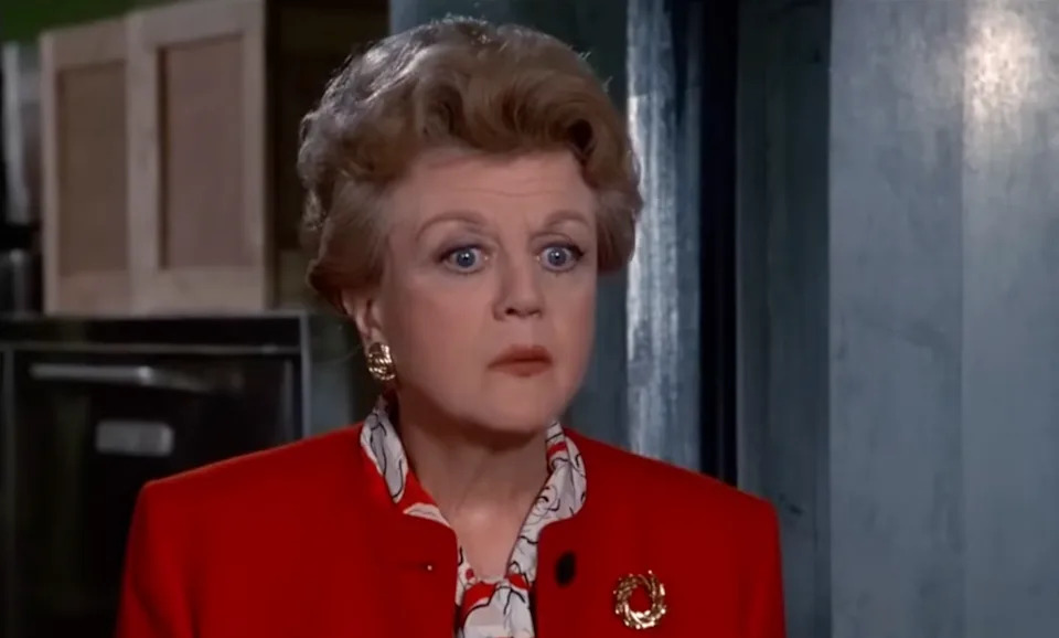 Jessica Fletcher (Angela Lansbury) is wearing a red jacket with a patterned blouse underneath, looking surprised or concerned