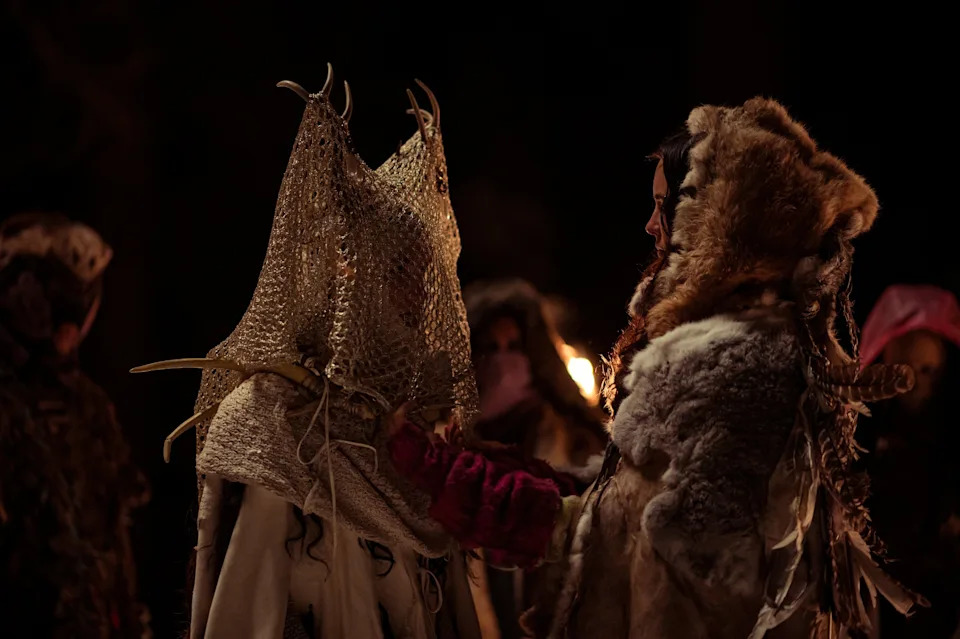 People wearing fur-lined costumes with ornate antler headdresses in a dramatic setting