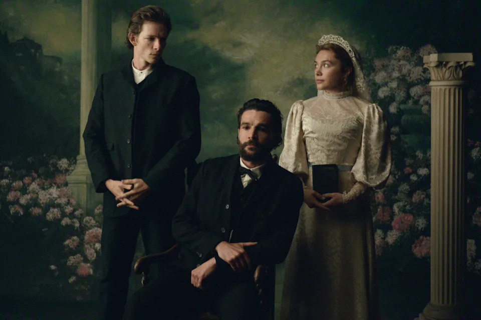 Three people in vintage attire pose in a formal portrait setting, styled in late 19th-century clothing with suits and a lace dress