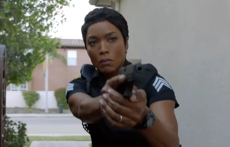 Athena Grant (Angela Bassett) aims a handgun intently, standing outdoors near a building