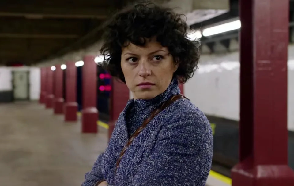 Dory Sief (Alia Shawkat) stands on a subway platform, looking to the side with a serious expression, wearing a textured jacket