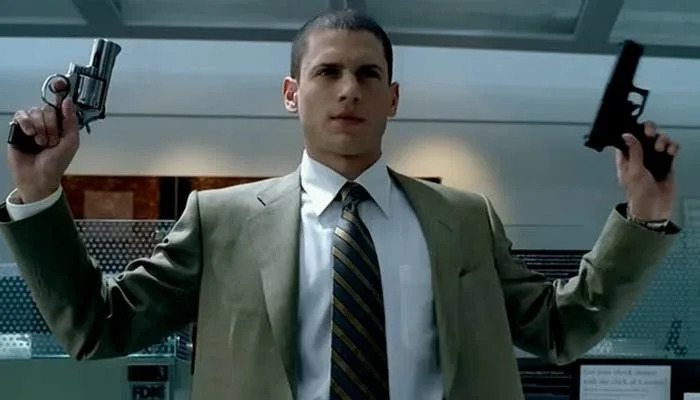 Michael Scofield (Wentworth Miller), in a suit, holds a revolver and a pistol inside an office setting, looking determined